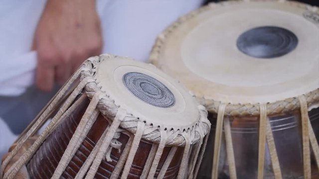 Video of a man's hands (wearing beads) playing the Tabla - Indian classical music percussion instrument - black background.
