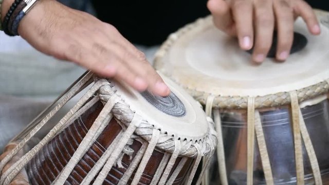 Video of a man's hands (wearing beads) playing the Tabla - Indian classical music percussion instrument - black background.