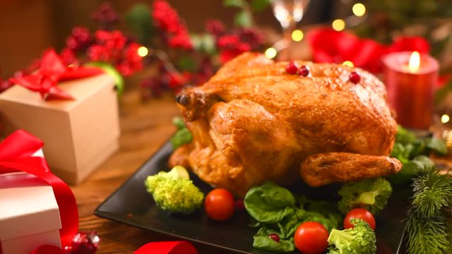 Christmas dinner. Roasted chicken on holiday table, decorated with gifts and burning candles. Roasted turkey over holiday background. Dolly shot, 4K UHD video footage 3840X2160