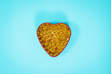 Top view of a heart shaped box with tablets in the middle on a blue, pastel background. Medical concept, care for the heart, eating pills strengthening the heart. Prevention of heart attack,.