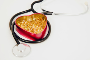 A heart-shaped box with tablets inside and a stethoscope. Medical concept, care for the heart, eating pills strengthening the heart. Prevention of heart attack, hypertension.