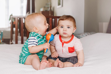 Group portrait of two white Caucasian cute adorable funny baby boys sitting together on bed communicating and playing. Friendship childhood concept. Best friends forever. Children fighting screaming