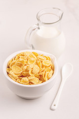 Crispy corn flakes in bowl with jar of milk
