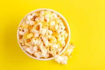 Tasty salty popcorn in paper cup on bright yellow backgraund