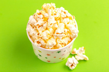 Tasty salty popcorn in paper cup on bright green backgraund