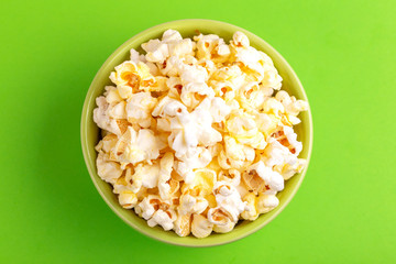 Tasty salty popcorn in bowl on bright green backgraund