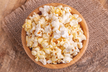 Tasty salty popcorn in wooden bowl on burlap napkin