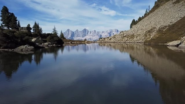 Low level flight over lake Spiegelsee (Mirror Lake) with reflections of the Dachstein mountains. Reiteralm, Schladming-Dachstein, Austria.