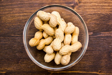 Peanuts on bowl on a wooden table viewed from above