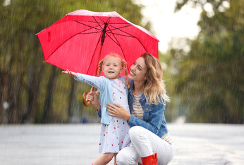 Portrait of happy mother and daughter with red umbrella in city on rainy day