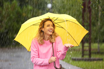 Portrait of young woman with yellow umbrella in park on rainy day