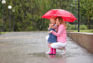 Happy mother and daughter with red umbrella in park on rainy day. Space for text