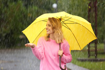 Portrait of young woman with yellow umbrella in park on rainy day