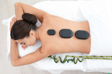 Beautiful young woman getting hot stone massage in spa salon, top view
