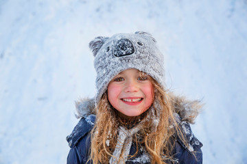 Cute little girl wearing navy jacket and knitted hat playing with snow in winter park. Child...