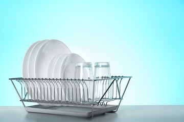 Drying rack with clean dishes and glasses on table against color background. Space for text
