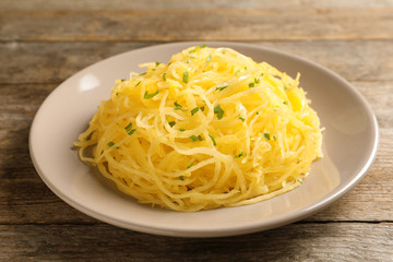 Plate with cooked spaghetti squash on wooden table