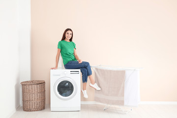 Young woman sitting on washing machine at home, space for text. Laundry day