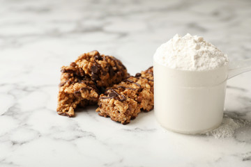 Tasty protein bars and scoop of powder on marble table