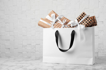 Paper shopping bag with handles full of gift boxes on table. Mock up for design