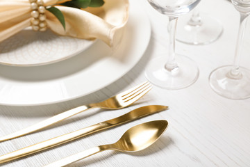 Golden cutlery and plates with napkin on wooden background, closeup. Festive table setting