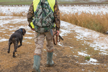 Hunter with a gun and a dog go on the first snow in the steppe, Hunting pheasant in a reflective...