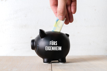 Hand legt Geld in Sparschwein, mit der Aufschrift 