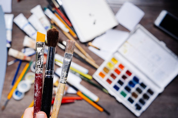 on the table are scattered art supplies, colorful watercolor paints, pencils, gouache, tubes with...