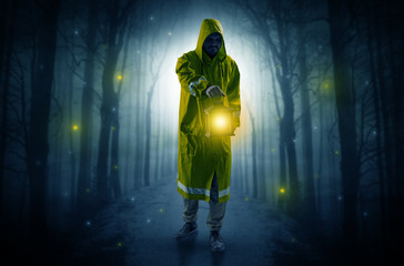 Man in raincoat coming from dark forest with glowing lantern in his hand concept
