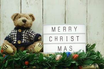 merry Christmas word on light box with teddy bear and green tinsel decoration