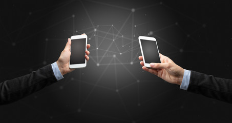 Close up of two hands holding smartphones to each other, wireless connection concept