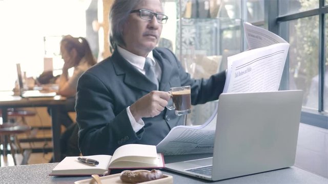Senior businessman with computer laptop. He spend their free time reading newspaper and drinking coffee, sit in a coffee shop, morning.