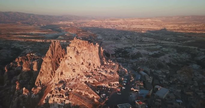 High angle aerial drone orbiting view clockwise around Uchisar Castle and otherworldly fairy chimney landscape valley in Cappadocia, Turkey. 4K at 23.97fps