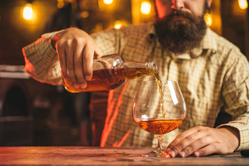 Barman pours whiskey, brandy or cognac. Pub retro vintage interior. Hipster barman concept. Swag guy with alcohol. Drunk man.