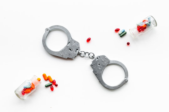 Arrest for illegal purchase, possession and sale drugs concept. Drugs as pills near handcuff on white background top view copy space pattern