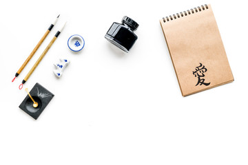 Chinese or japanese calligraphy pattern. Hieroglyph love in craft paper notebook and writing accessories on white background top view space for text