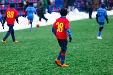 Young Active sport heathy boys in red and blue sportswear running and kicking a red ball on football field with artificial turf. soccer youth team plays football. activities for kids, training