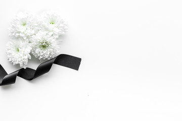 Funeral symbols. White flower near black ribbon on white background top view space for text
