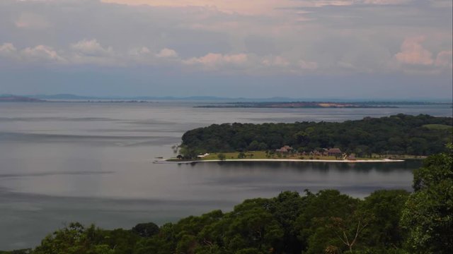 View of Ssese Islands in Lake Victoria from hill in Kalangala, Uganda (Time lapse). Gusts of wind on still water. Forest, peninsula, far away islands, cloudy blue sky and horizon showing.
