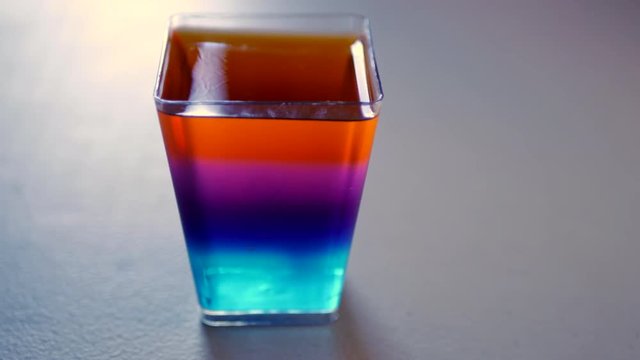Rainbow jelly in a rectangular shaped cup. Slide from left to right. Colourful desert for a kids birthday party.
