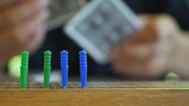 Close up of picking cards on a table behind a row of cribbage pegs.