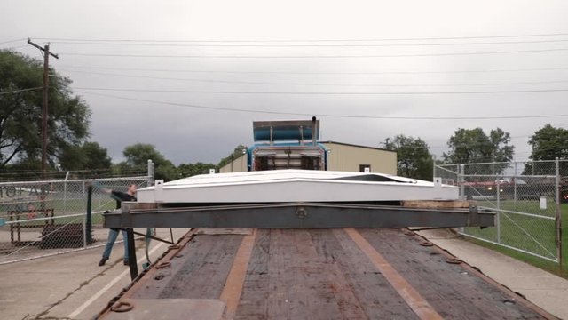 Young man throwing winch strap to other side of flatbed trailer to secure oversized cargo in slow motion.