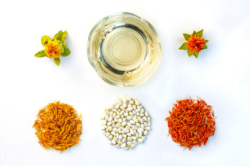 Yellow, red dried petals, inflorescences, seeds and oil of safflower against a white background. View from above. Flat lay. - obrazy, fototapety, plakaty