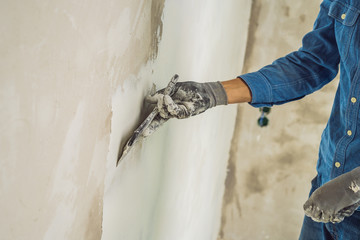 master is applying white putty on a wall and smearing by putty knife in a room of renovating house in daytime