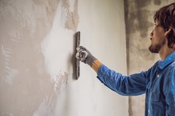 master is applying white putty on a wall and smearing by putty knife in a room of renovating house...