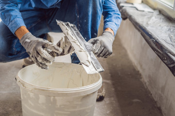 master is applying white putty on a wall and smearing by putty knife in a room of renovating house...