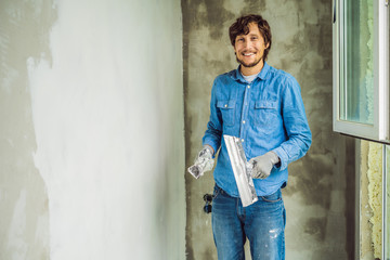 master is applying white putty on a wall and smearing by putty knife in a room of renovating house...