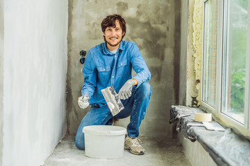master is applying white putty on a wall and smearing by putty knife in a room of renovating house...