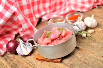 Raw pork meal diced in a old saucepan, garlic, half of onion, sweet pepper and checkered red tablecloth in the background
