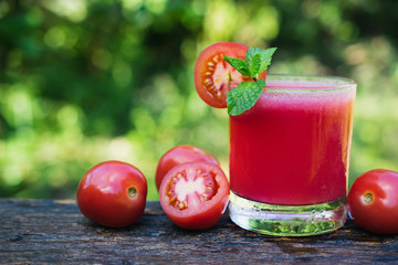 Tomato juice on wooden with tomato be side and mint leaves on top in nature background for healthy concept.